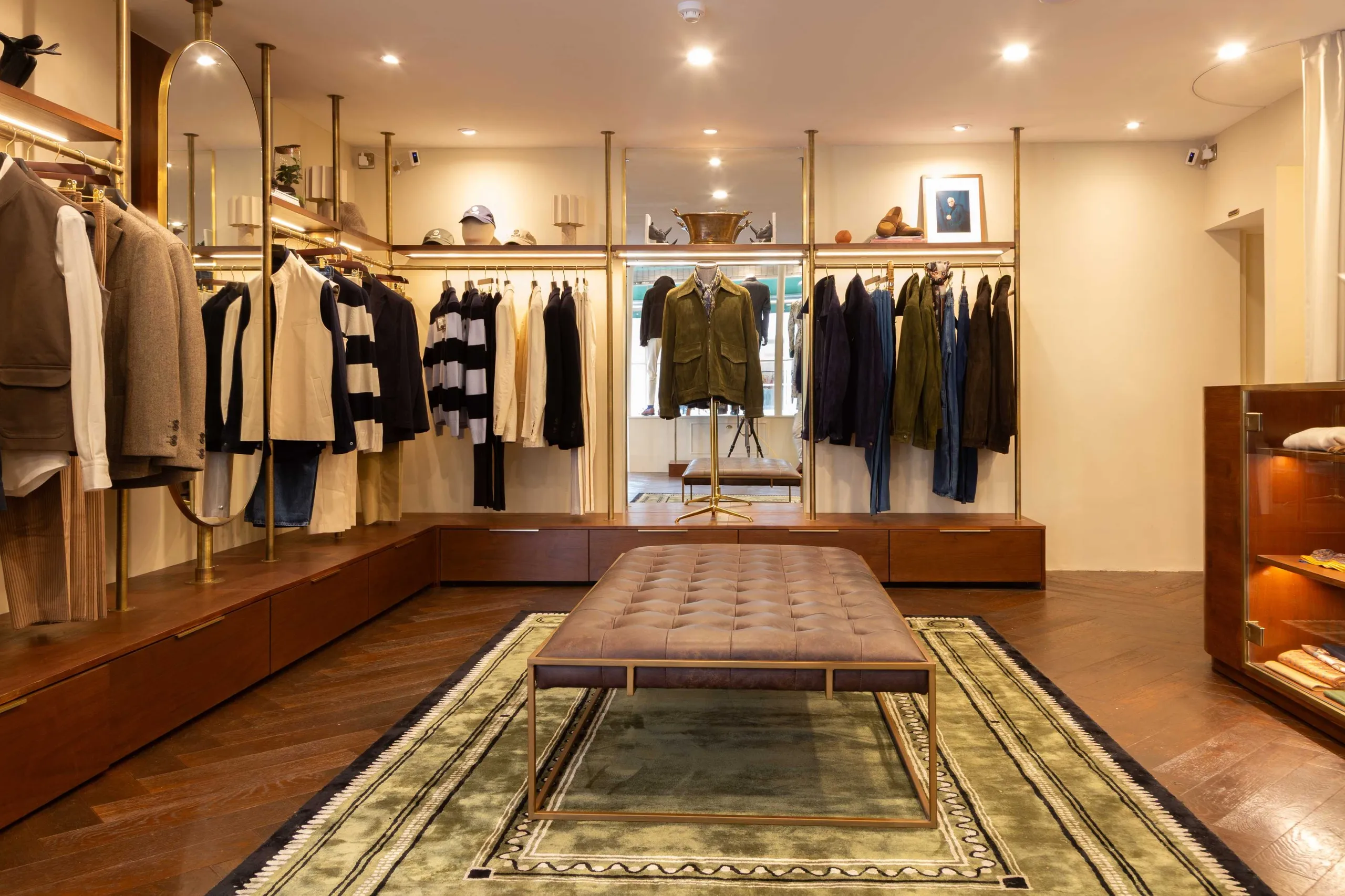 Menswear boutique with brass rails, timber cabinetry and a leather bench on a rug