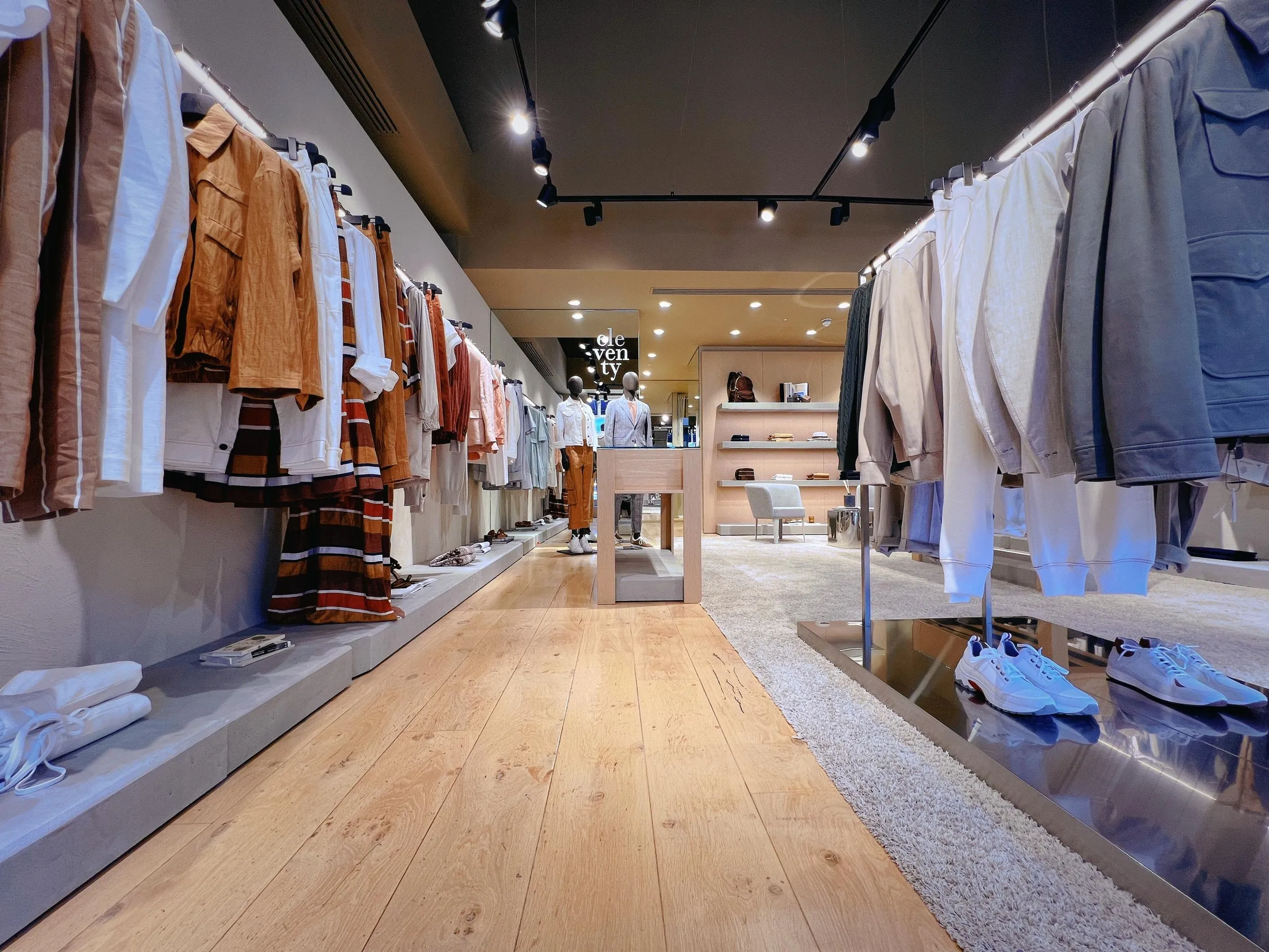 Eleventy menswear store with oak floor, steel shelving and pale stone walls
