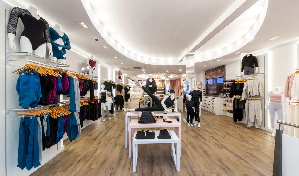 Bloch store with dancewear on wall rails, white display tables and a curved lit ceiling