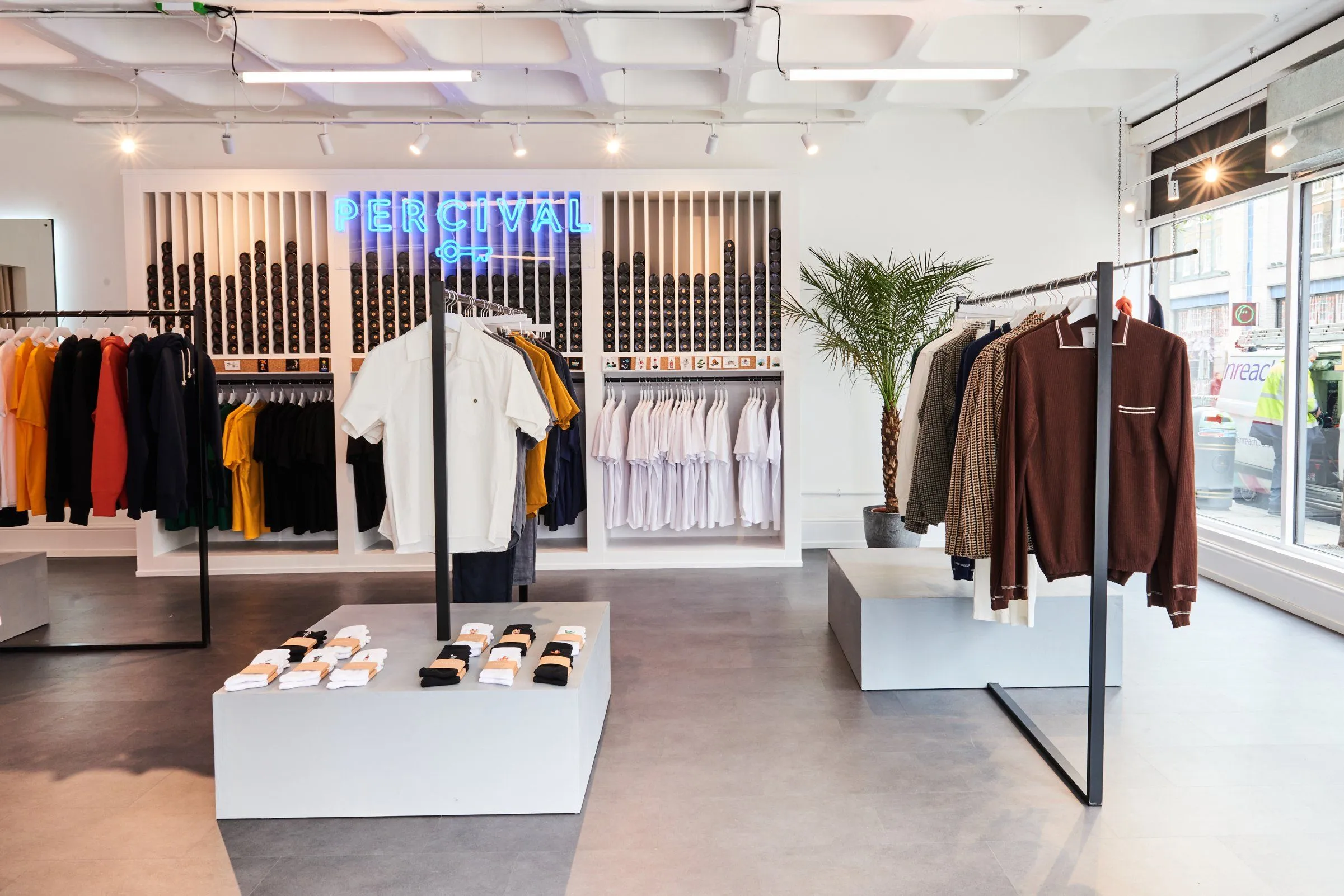 Percival pop-up store with clothing rails, a neon sign and white display plinth