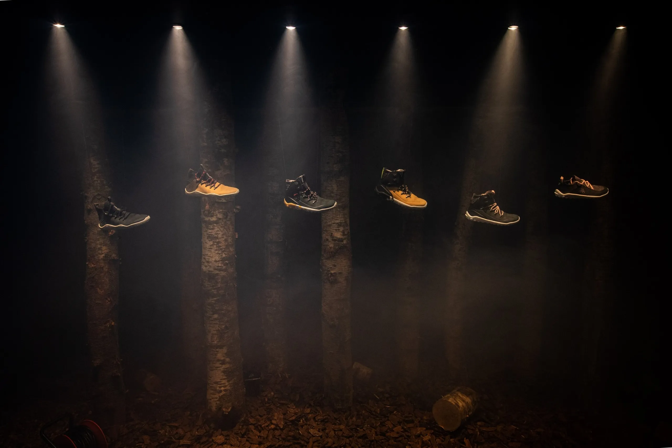 Footwear display with trainers lit above tree trunks in a dark forest scene