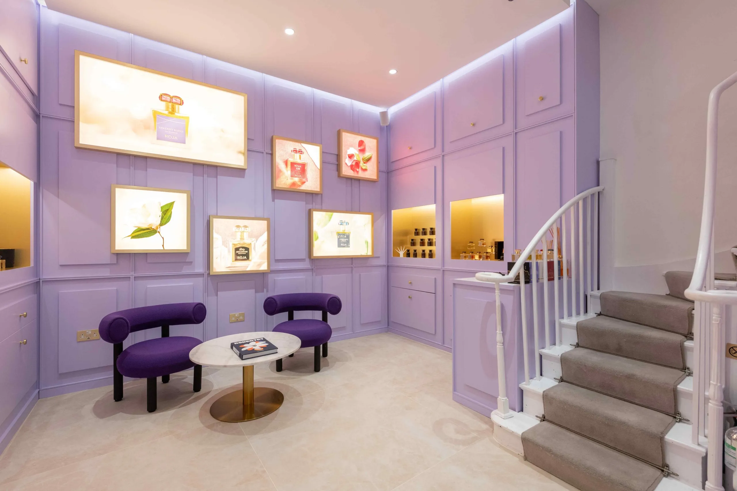 Roja lilac panelled room with backlit artworks, purple armchairs and a staircase
