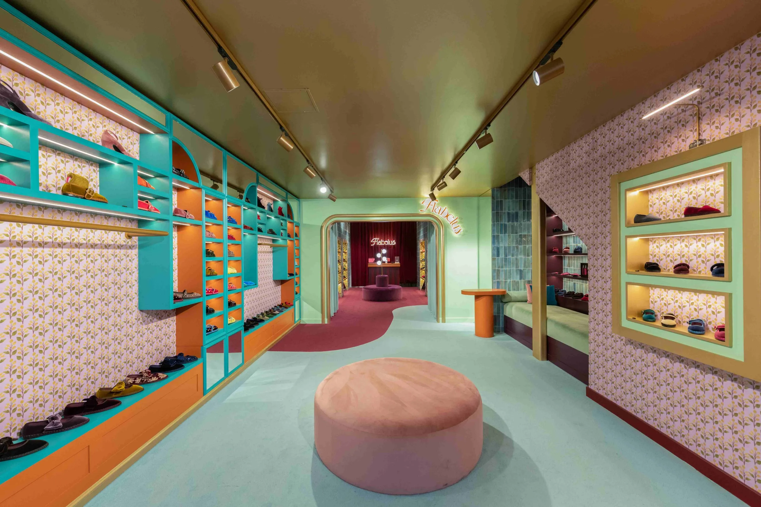 Flabelus store with patterned wallpaper, turquoise shoe shelving and a pink pouffe